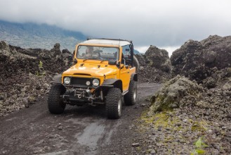 Afbeeldingen van A curly-haired man is looking away driving an offroad yelow vehicle at the top of a valley with dark ground road